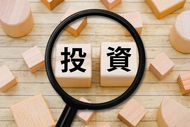 「投資」と書かれた木製ブロックを虫眼鏡で拡大している様子