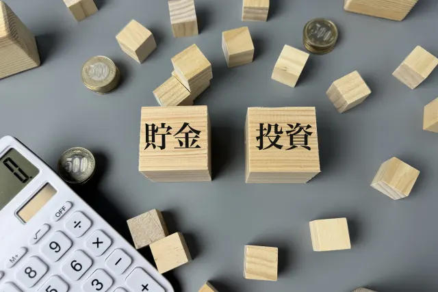 「貯金」と「投資」と書かれた木製ブロック、500円玉と電卓