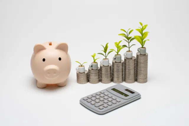 ピンクの豚の貯金箱と、少しずつ高くなる硬貨の山に植えられた若芽、電卓
